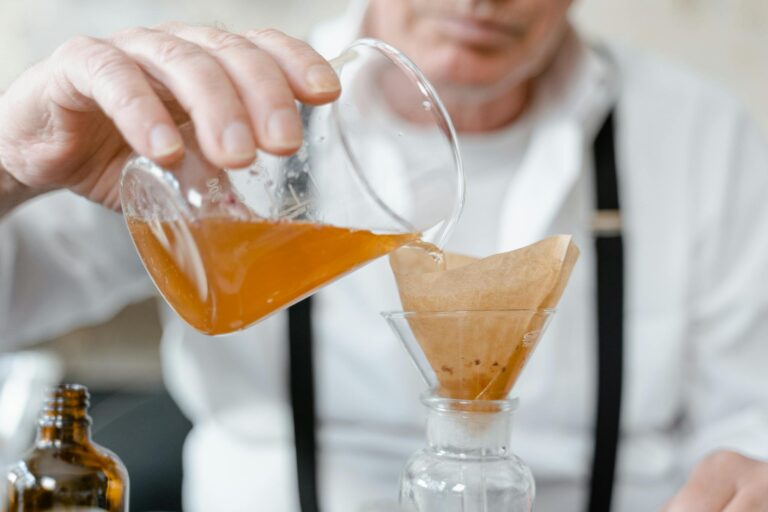 A scientist filters an orange liquid using a beaker and funnel in a laboratory setting.