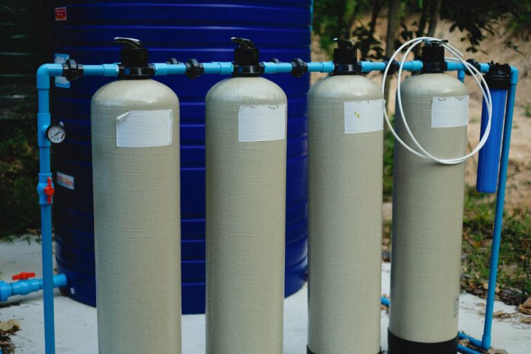 Four beige tanks in an outdoor water treatment setup with blue piping.