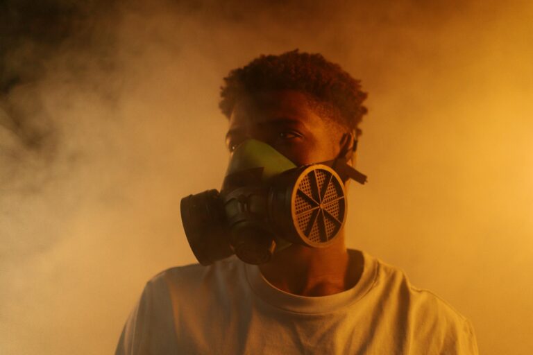 Portrait of a man wearing a gas mask surrounded by smoke with warm atmospheric lighting.